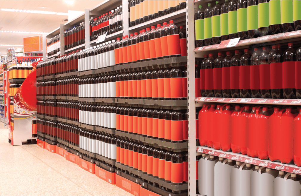 The beverage aisle in the grocery store shows 2-liter soda containers displayed on stacked pallets and shelves.