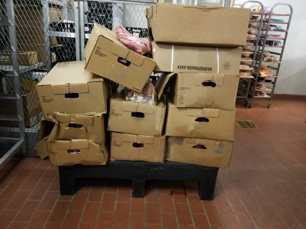 Damaged corrugated boxes have toppled over on a pallet, with meat falling out of the ripped sides and tops of the boxes in a store’s backroom.