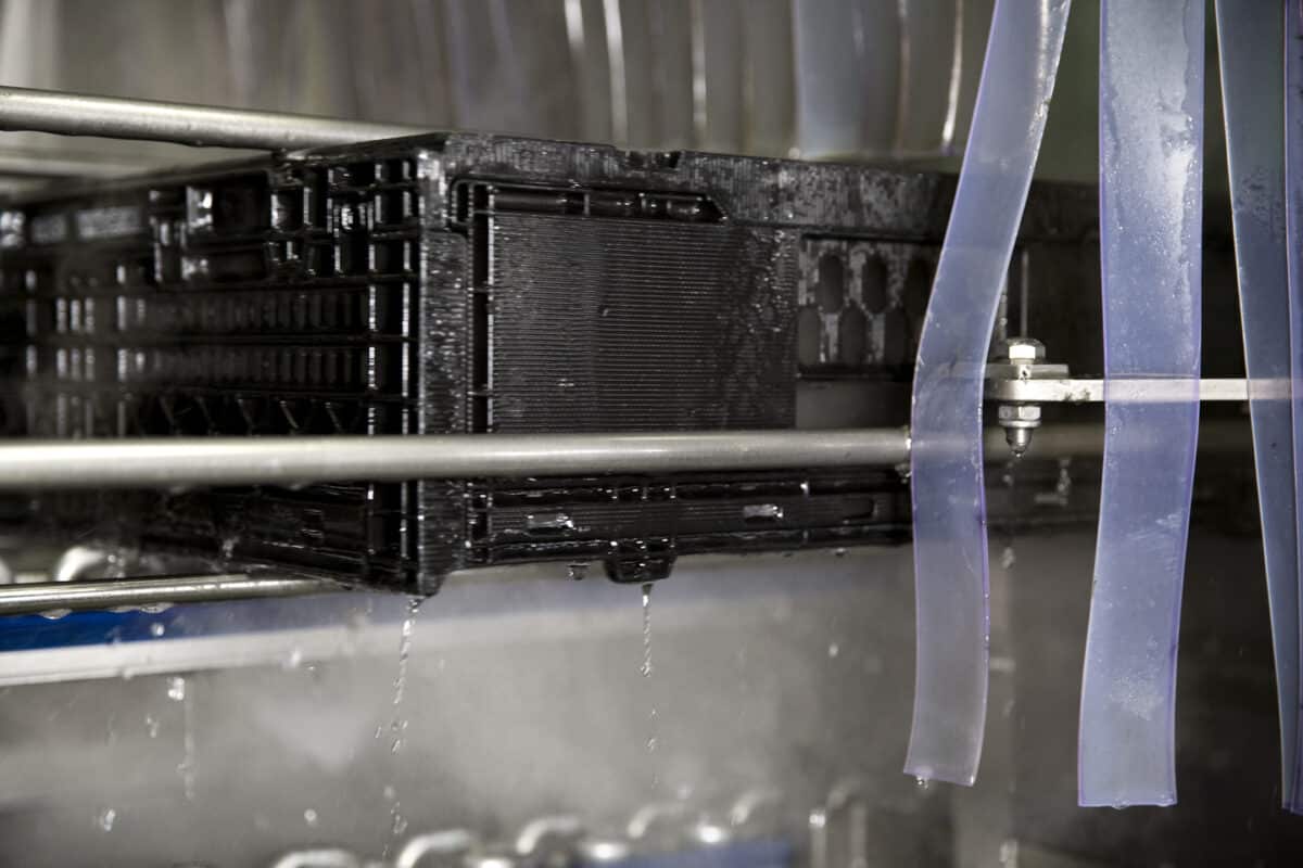 A freshly cleaned black plastic crate exiting an automated washer. Tosca ensures high food safety and quality assurance for optimal sanitation.