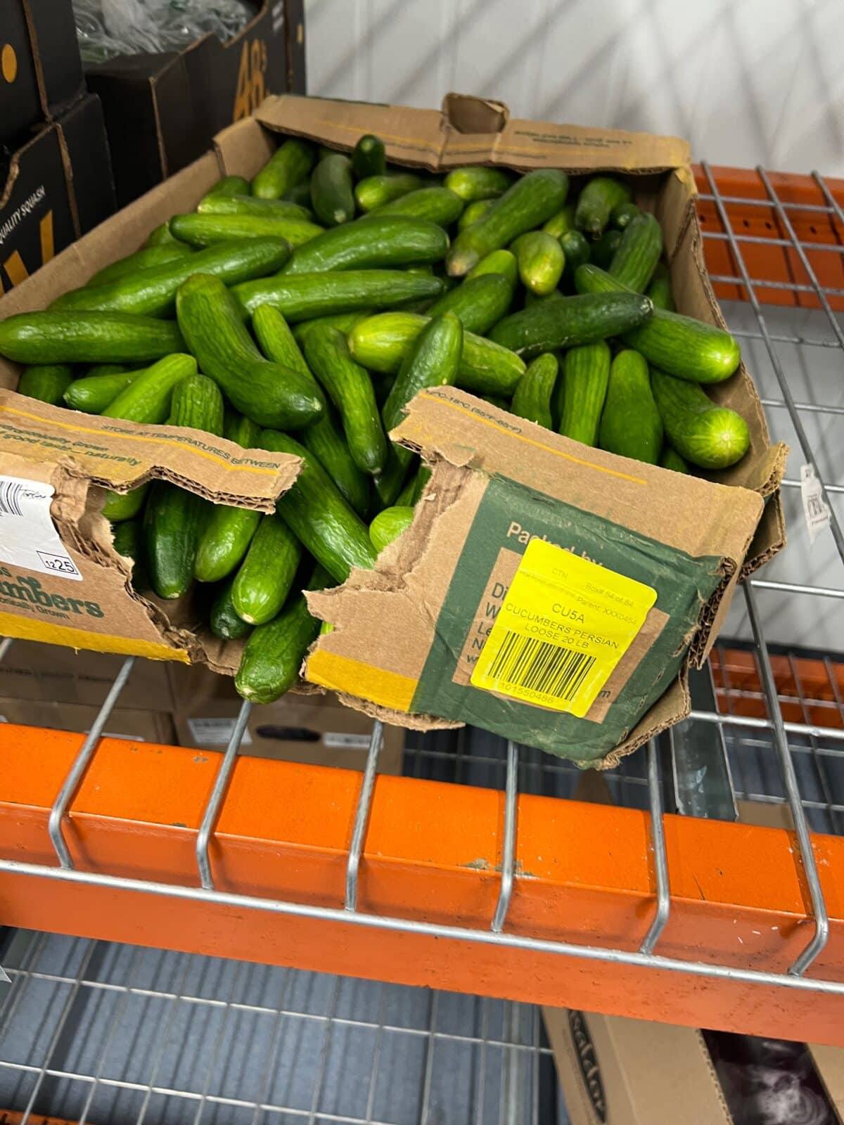 Damaged corrugated cardboard box of cucumbers with product falling out of ripped side.