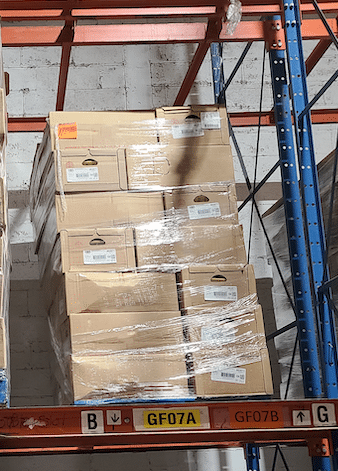 two pallets with corrigated boxes wrapped in shrink wrap sit racked inside of storage in a distribution center